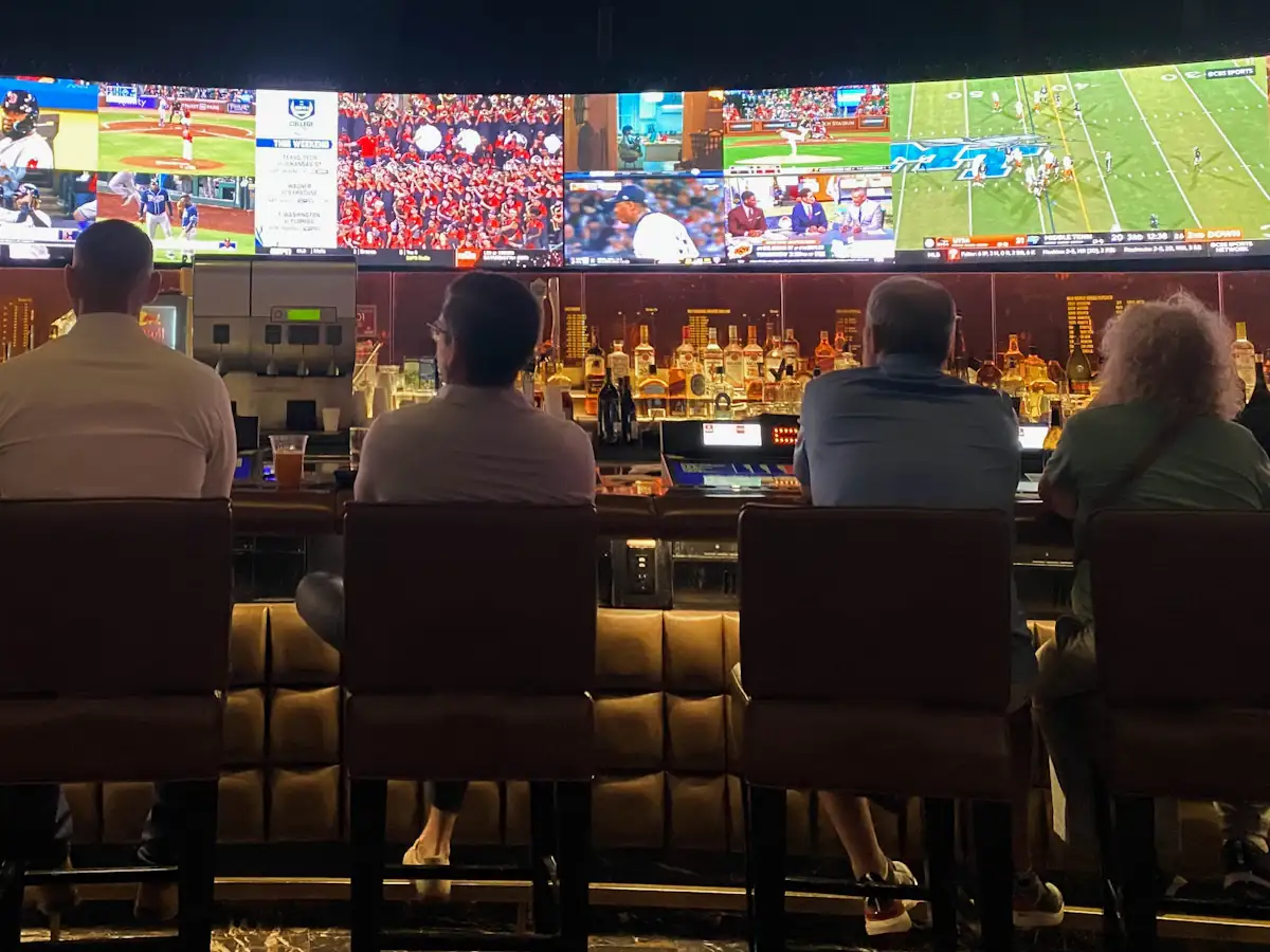 Guests on bar stools watching baseball and football on a wall of screens at a sports bar