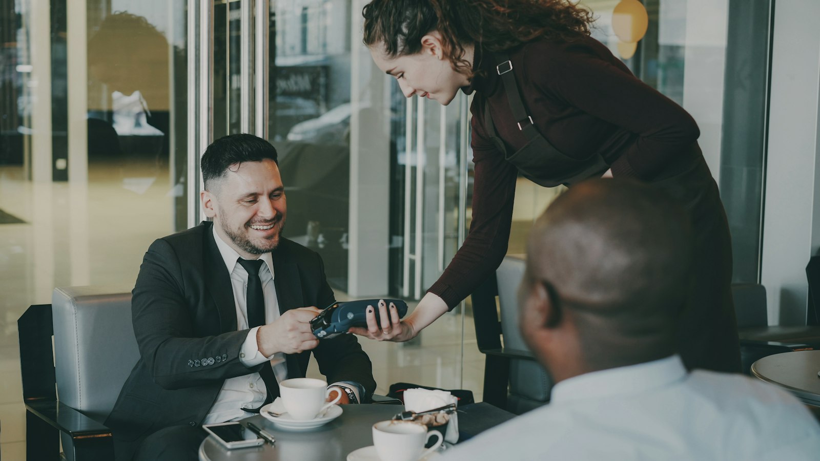 Server holding a card terminal for a guest paying at a cafe table